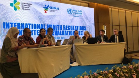 8 people sitting behind desks on stage, presenting in the meeting.